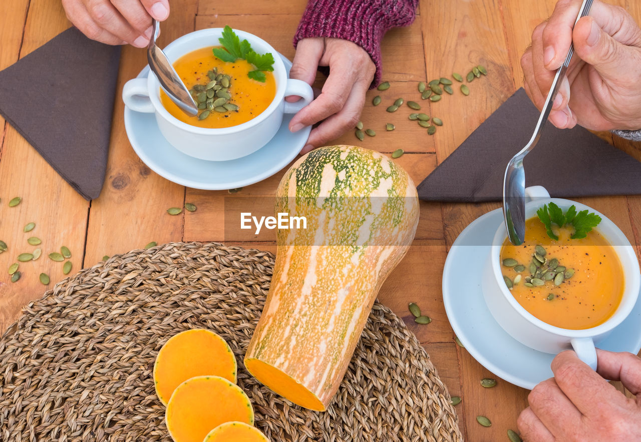 Cropped hands of people having pumpkin soup on table