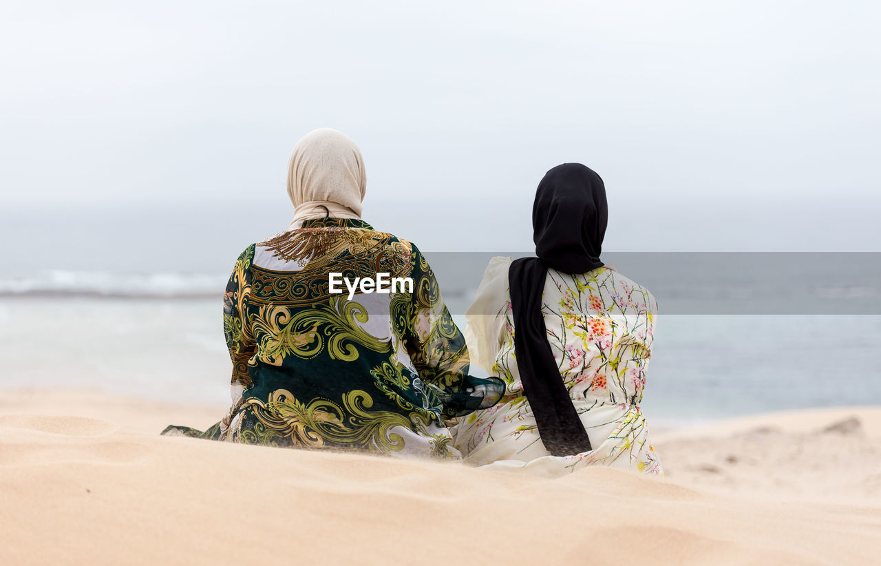 Rear view of women looking at sea while sitting on sand