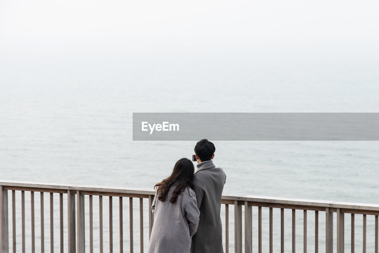 REAR VIEW OF WOMAN LOOKING AT SEA