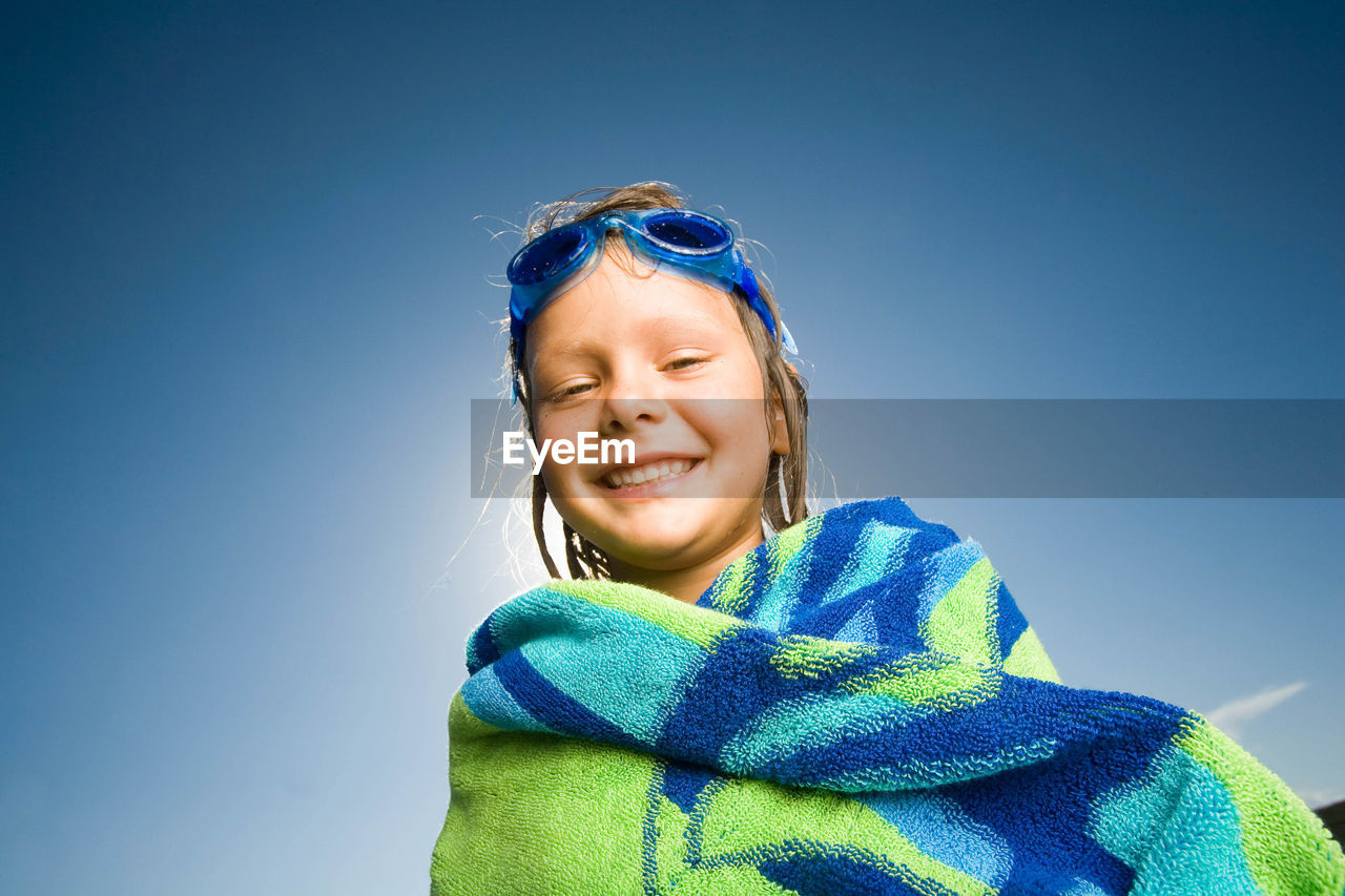 Portrait of happy girl covered with towel against blue sky