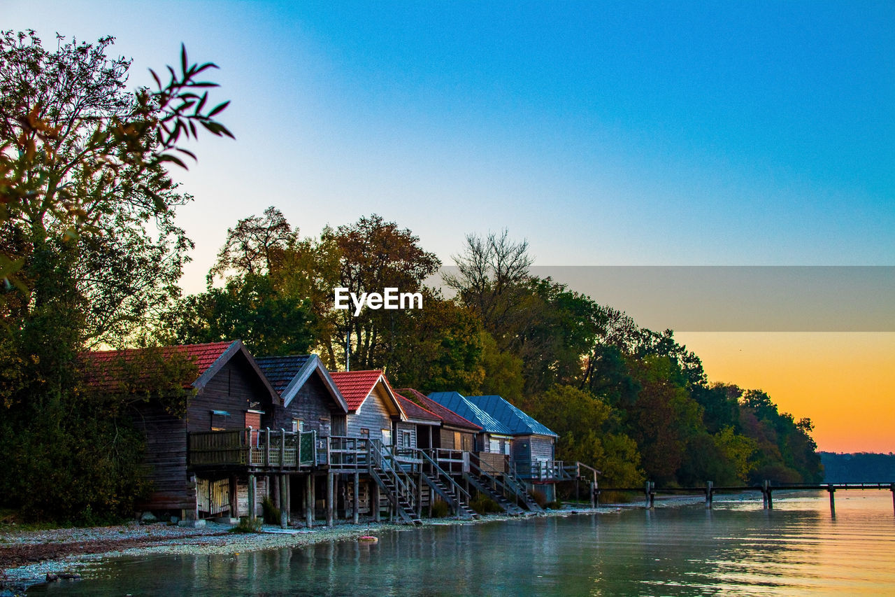 House and trees by lake against clear blue sky