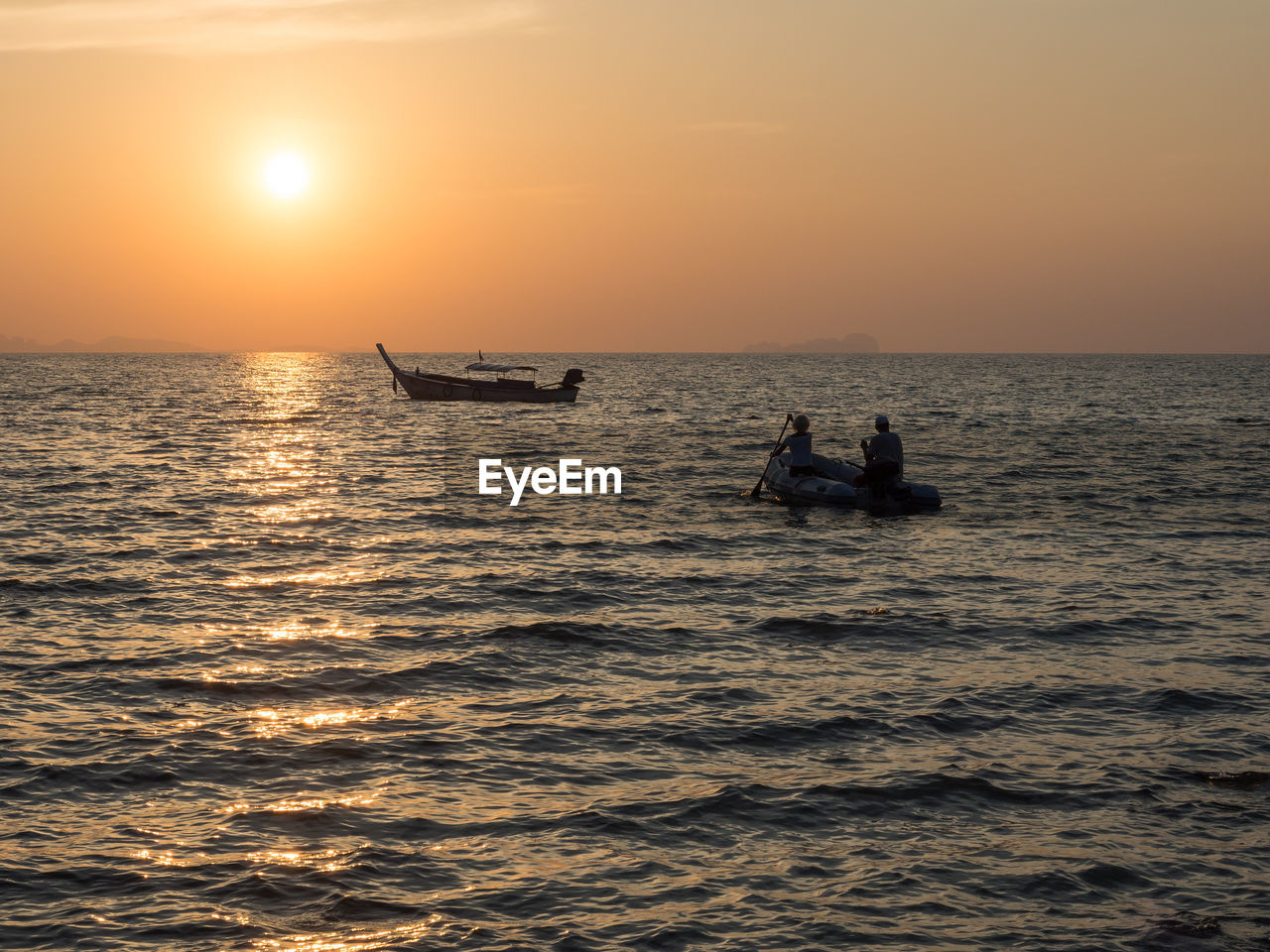 Silhouette of people in rowing boat on sea against sky during sunset