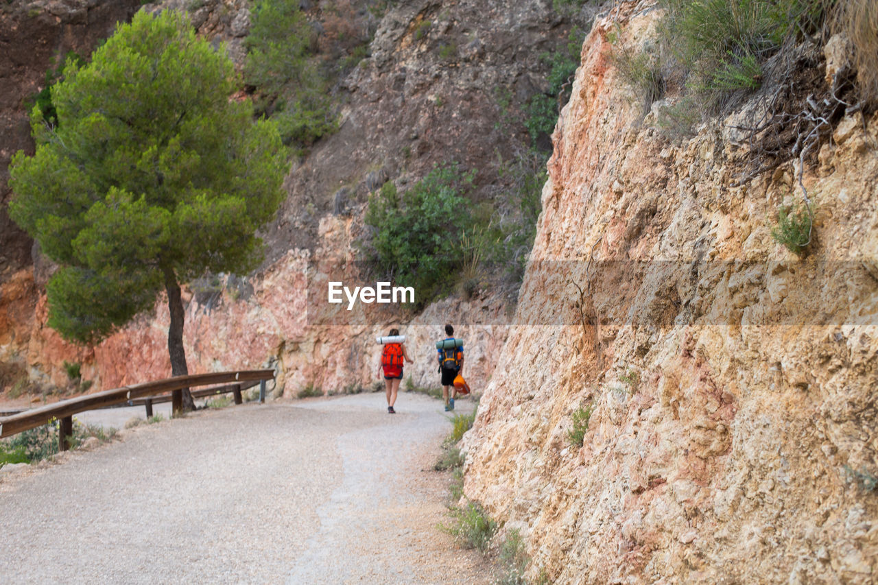 PEOPLE WALKING ON ROAD BY ROCK