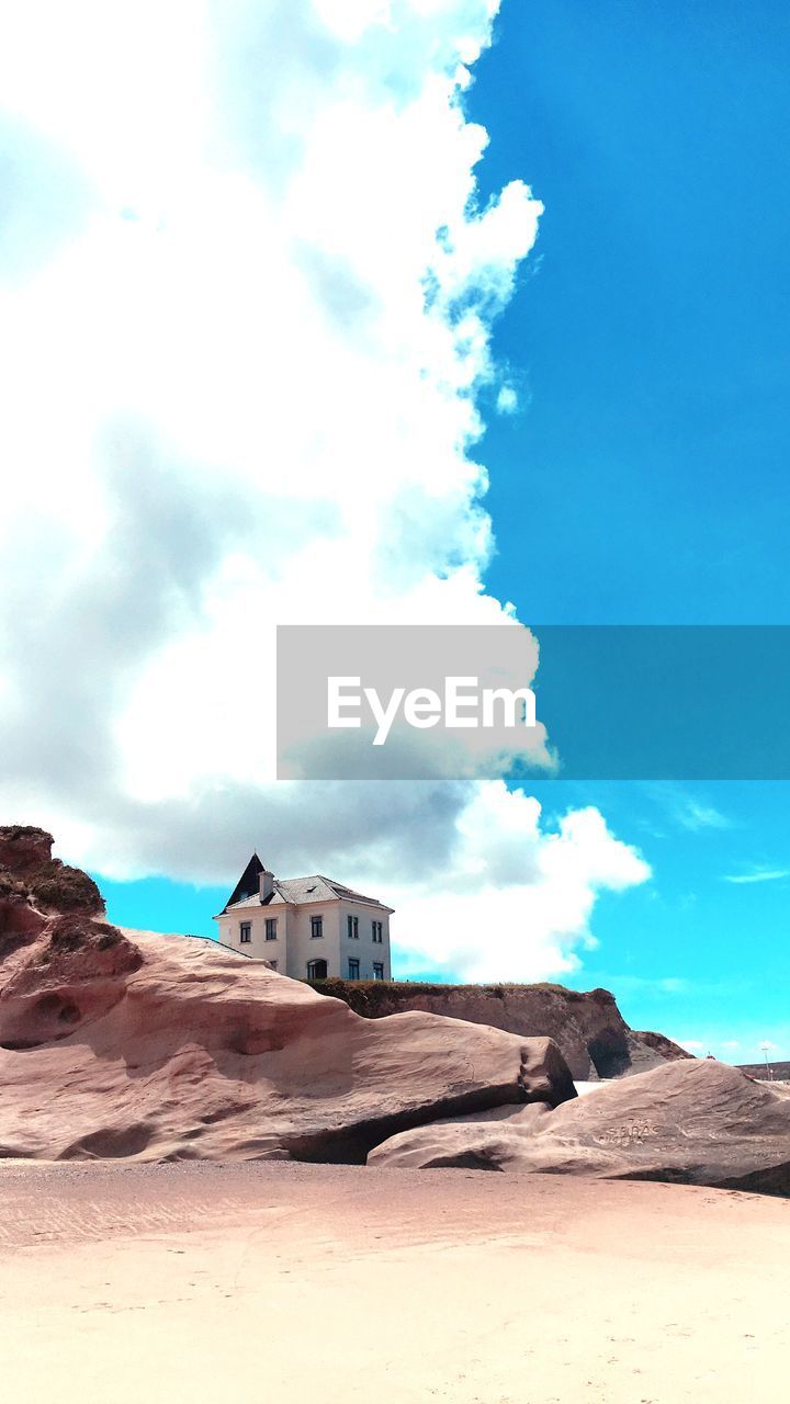 HOUSE ON SAND DUNE AGAINST SKY