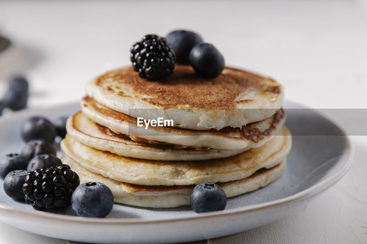 Stack of pancakes with berries on top on a white surface