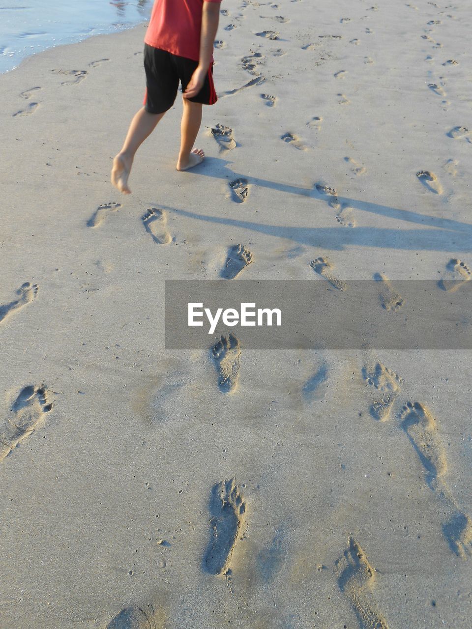 Low section of boy walking on sand at beach