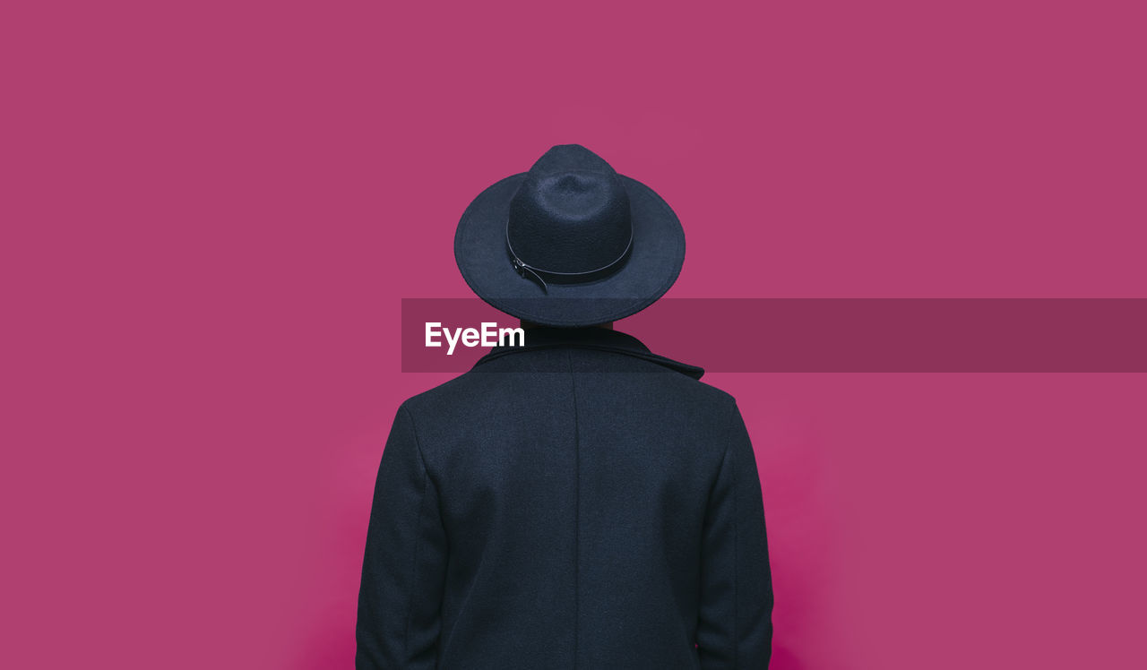 Man in hat standing in front of pink background