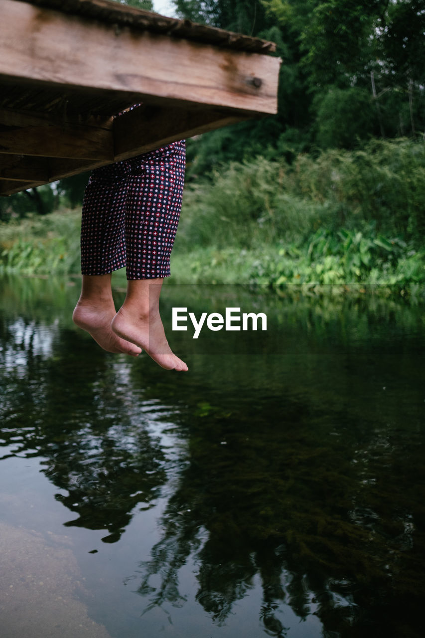 LOW SECTION OF WOMAN STANDING ON LAKE AGAINST TREES