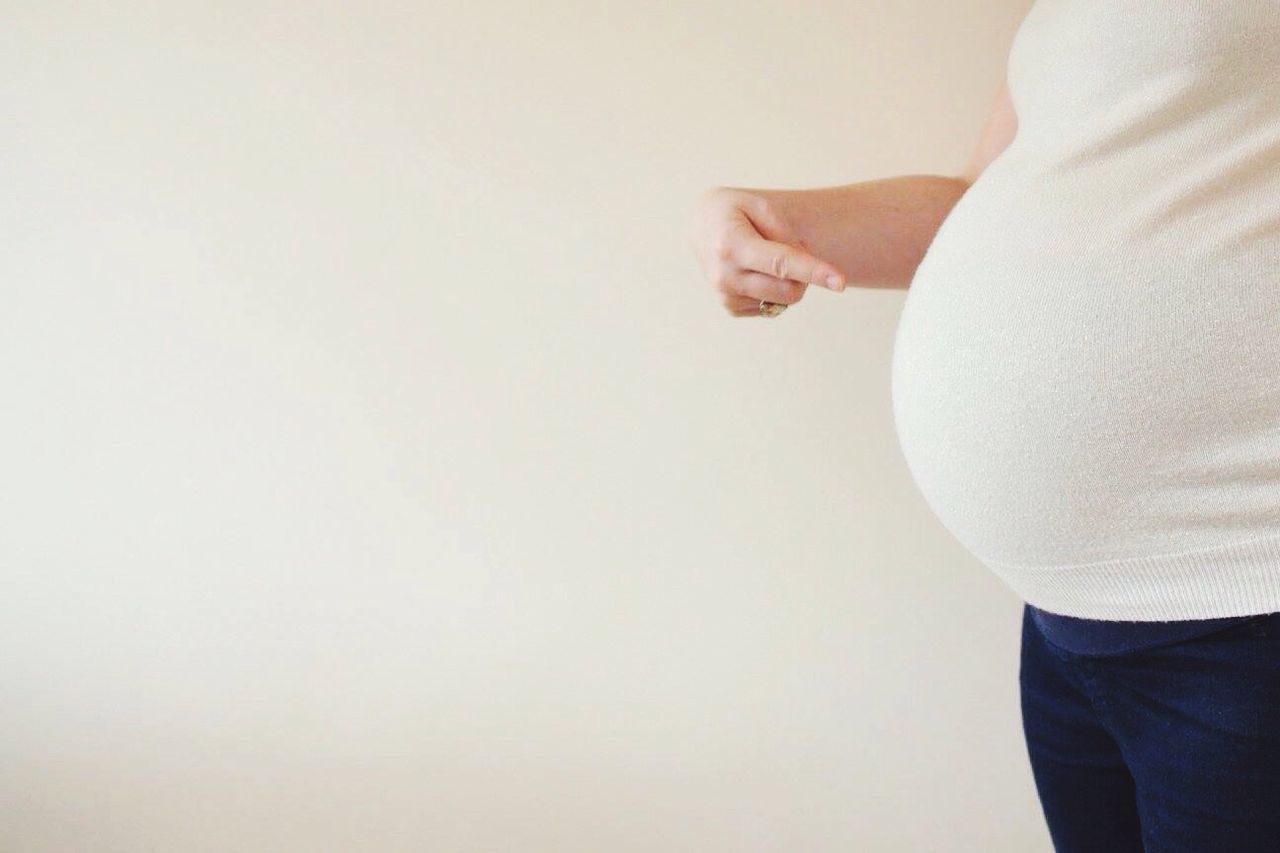 Pregnant woman gesturing towards stomach against white background