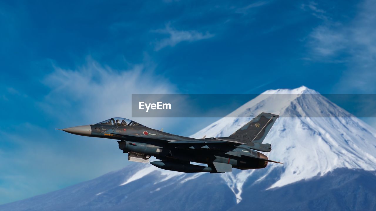 AIRPLANE FLYING OVER SNOWCAPPED MOUNTAIN AGAINST SKY