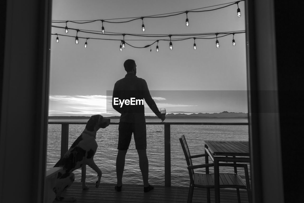 SILHOUETTE MAN WITH DOG STANDING AT SEA SHORE