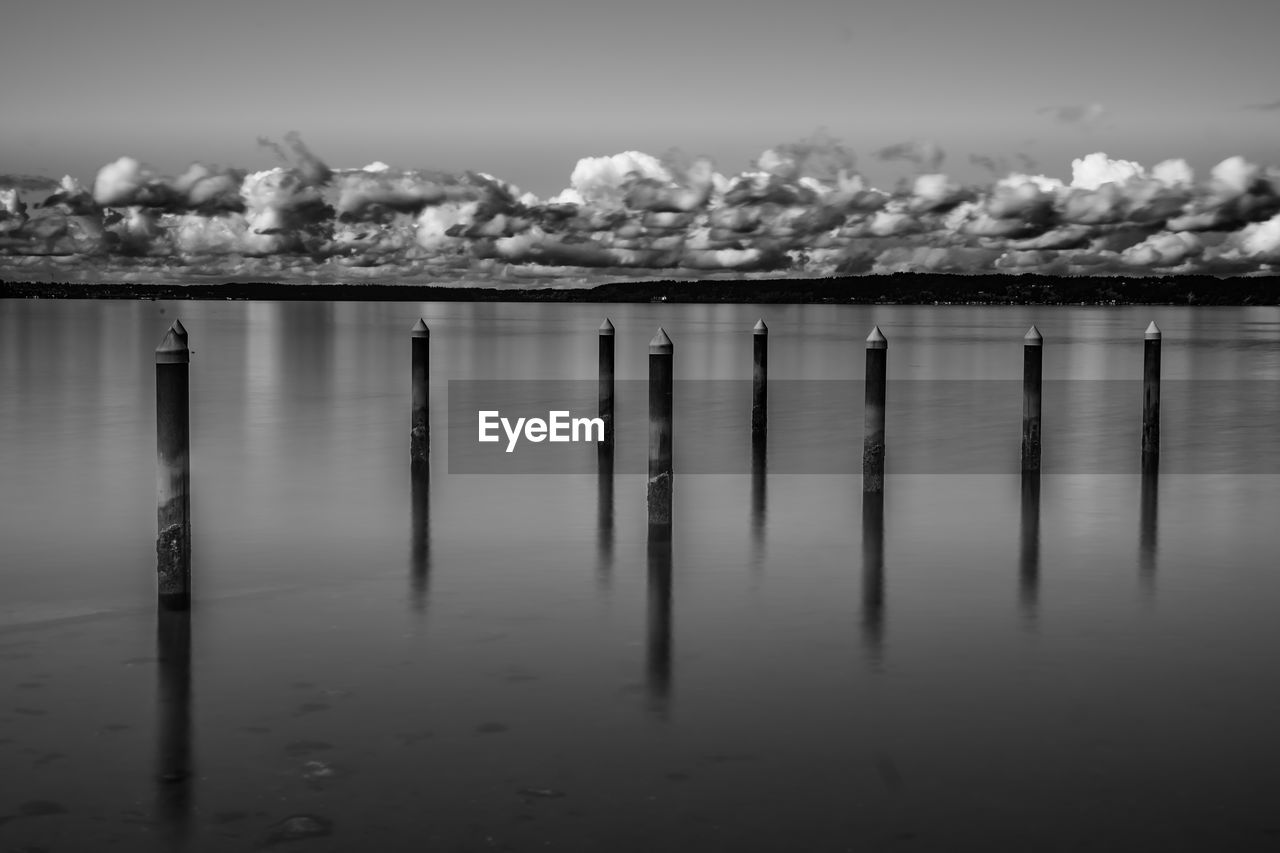 WOODEN POSTS ON LAKE AGAINST SKY