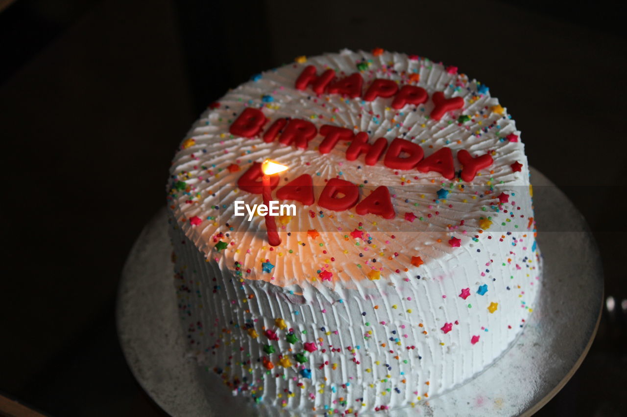Close-up of burning candle and text on birthday cake on table