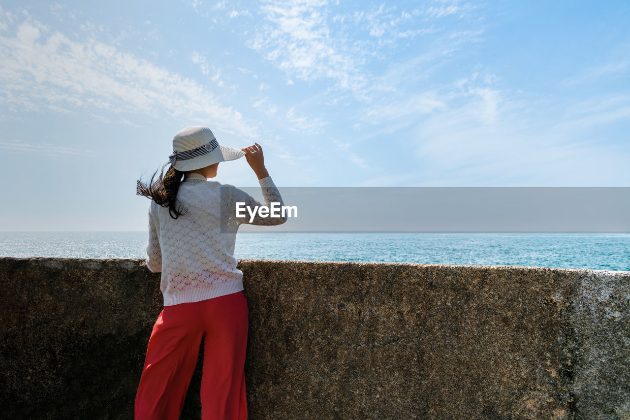 Rear view of woman standing at beach against sky