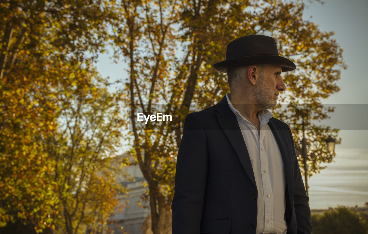 Portrait of adult man in suit and hat on street with autumn trees. madrid, spain