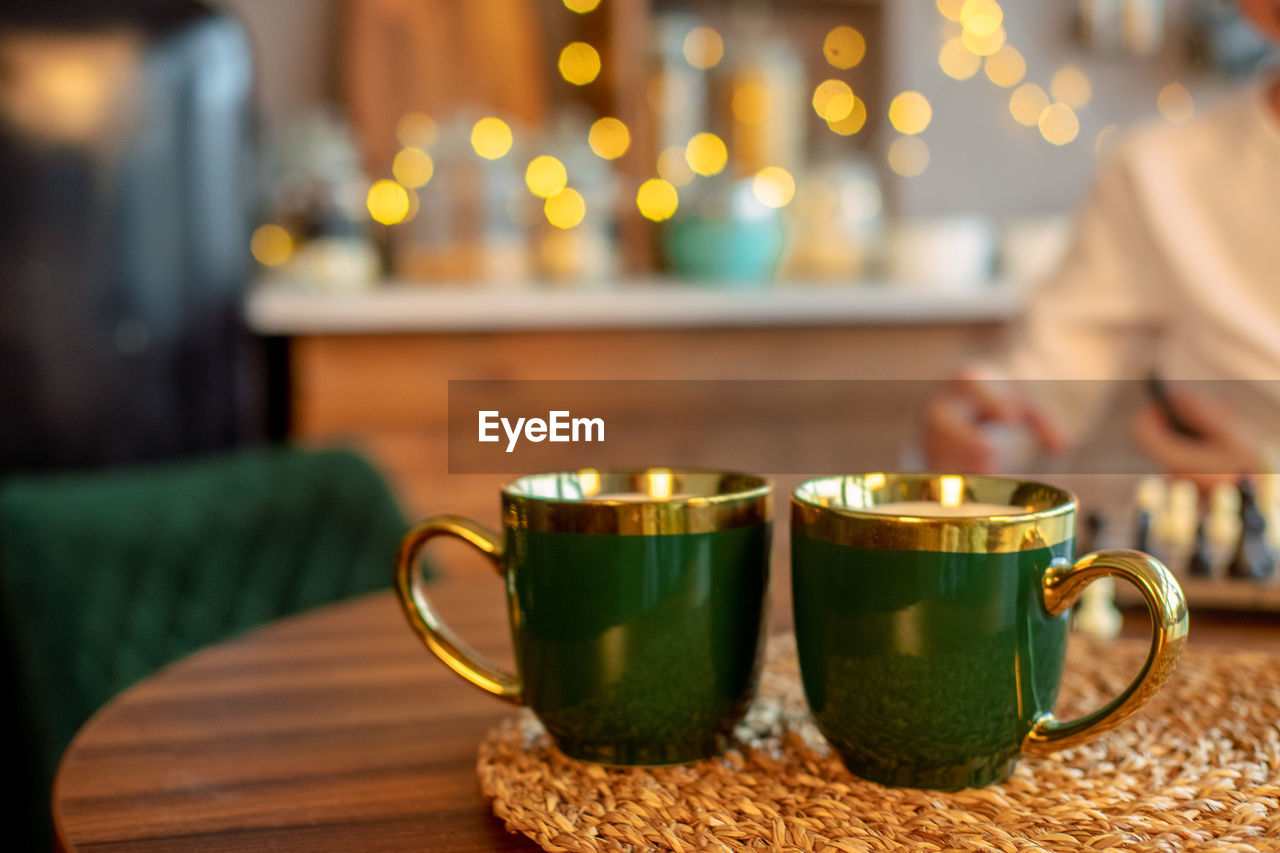 2 green cups close-up on a wooden table, against the background of garland lights