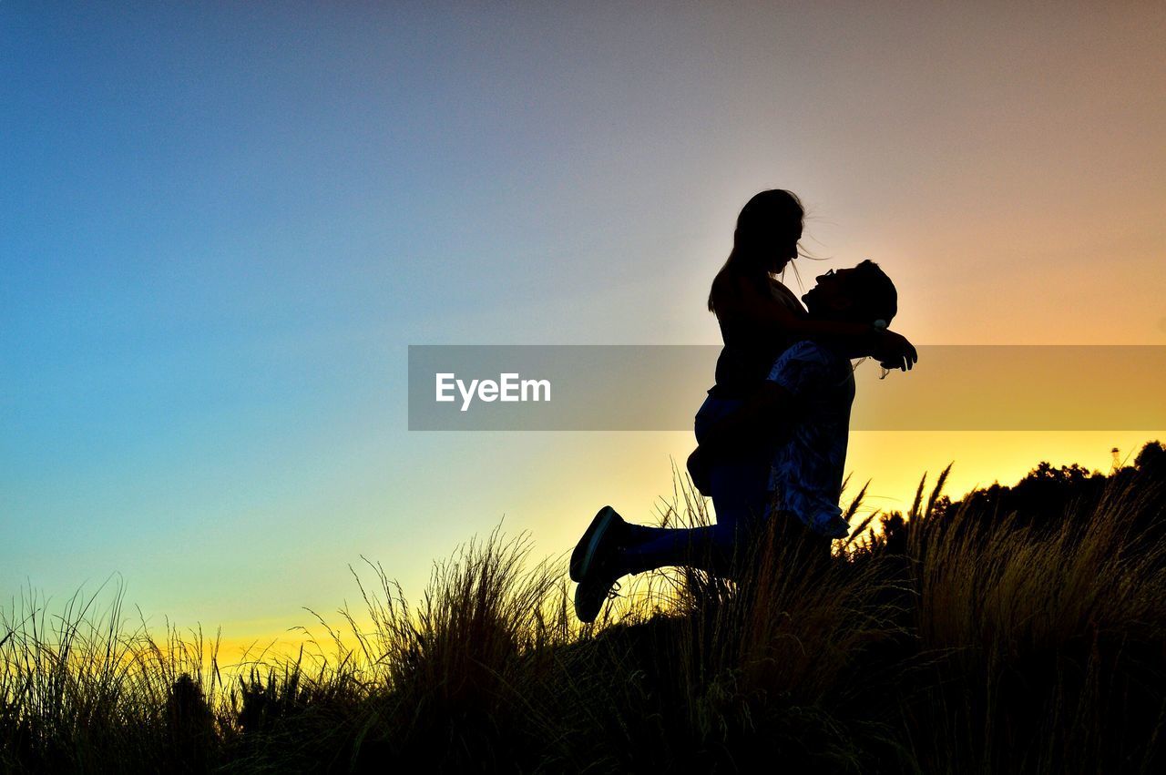 Silhouette couple on field against sky during sunset