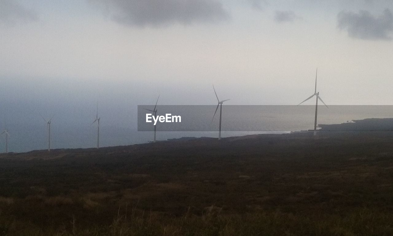 Wind turbines on landscape against cloudy sky