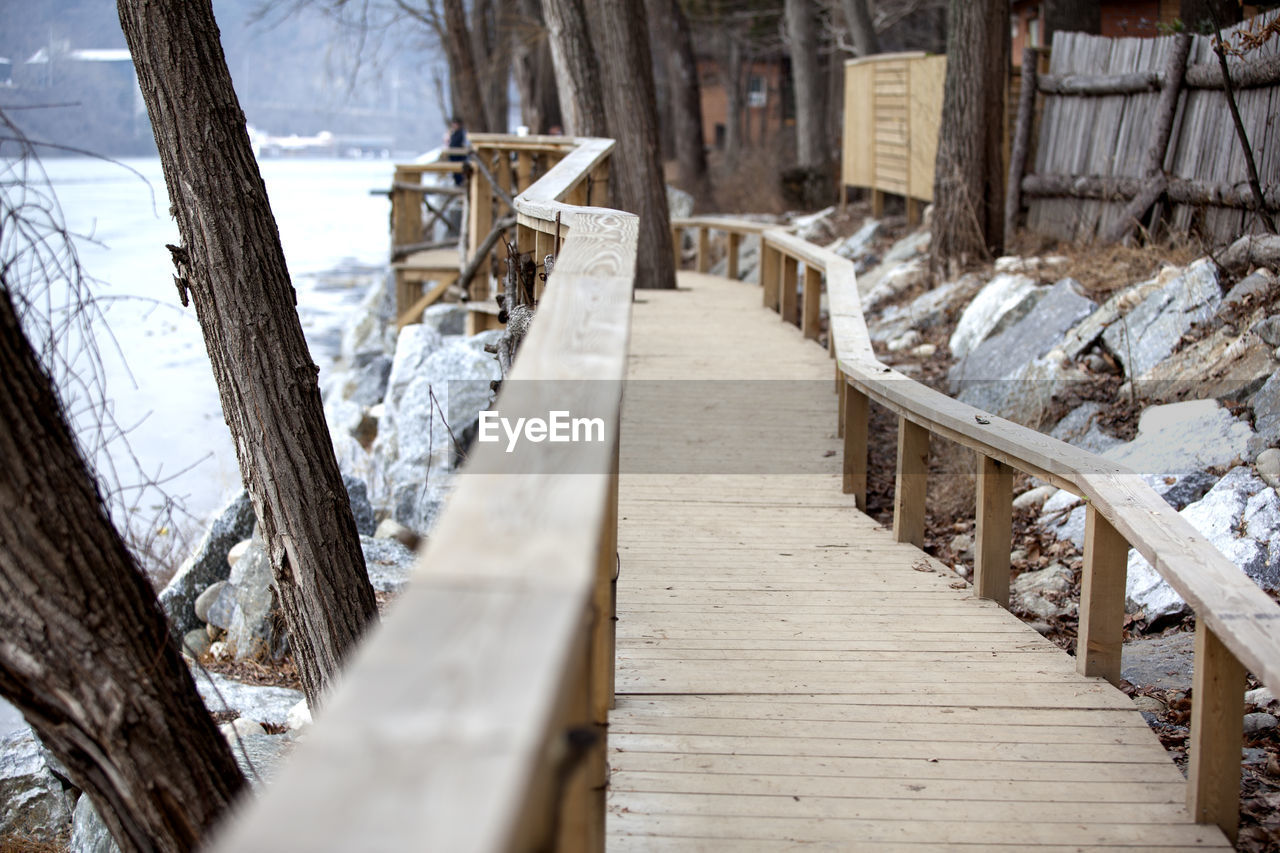 Wooden boardwalk by frozen river during winter