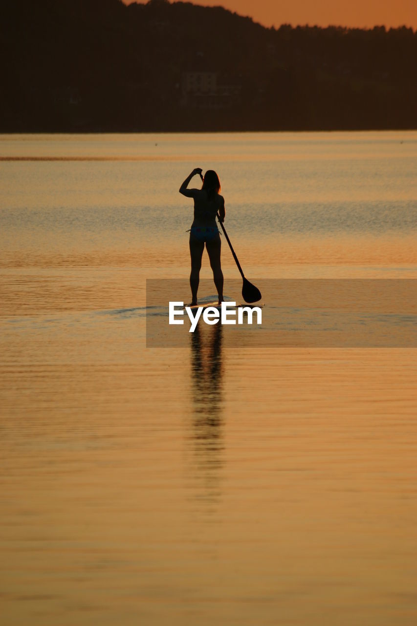 Silhouette woman paddleboarding at sea against sky during sunset