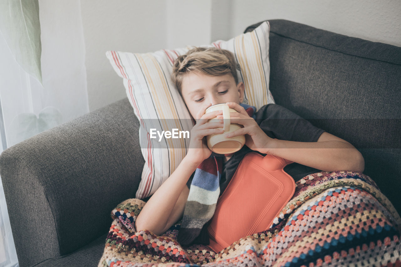 Ill boy having coffee while relaxing on sofa at home