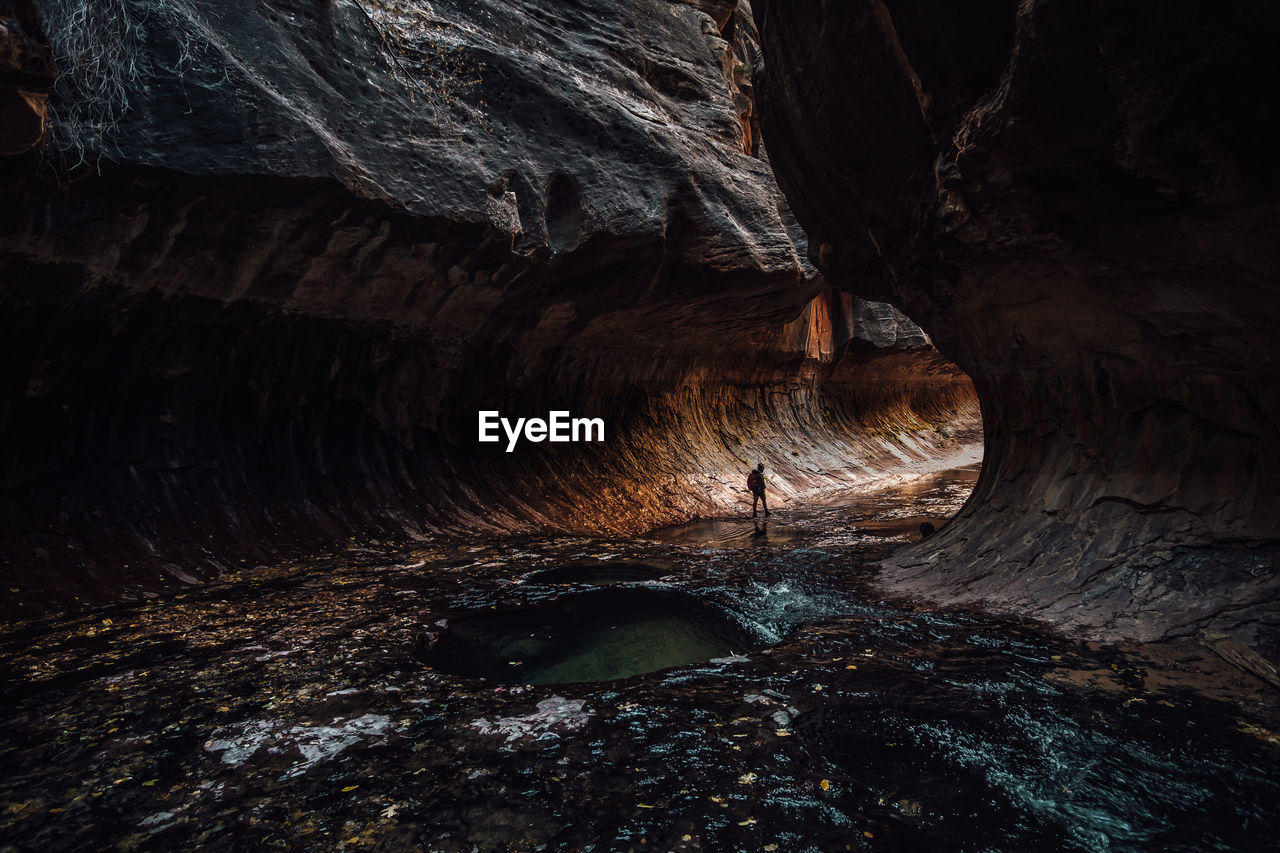 Silhouette woman walking by rock formation in cave