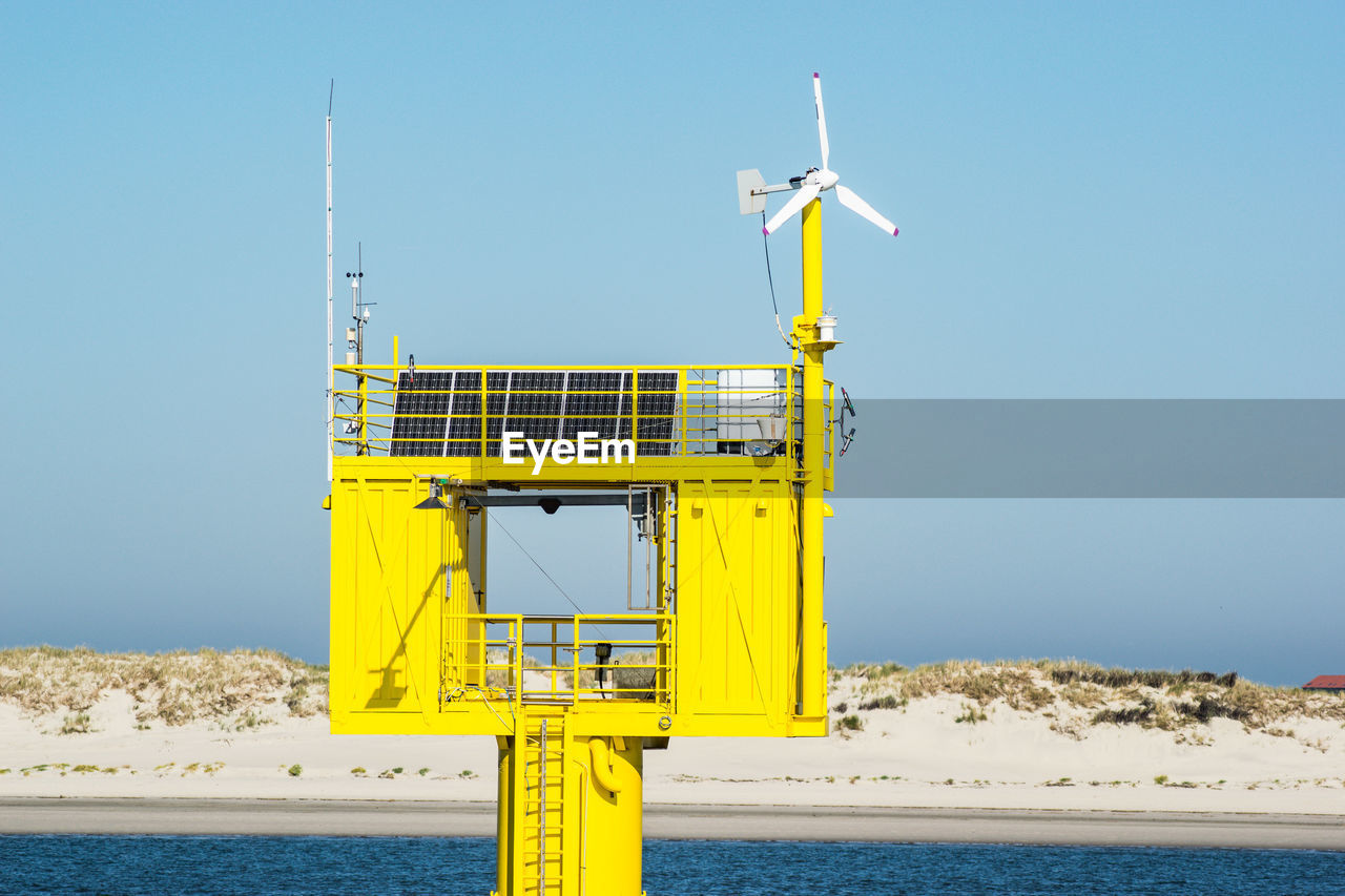 Information sign by sea against clear blue sky