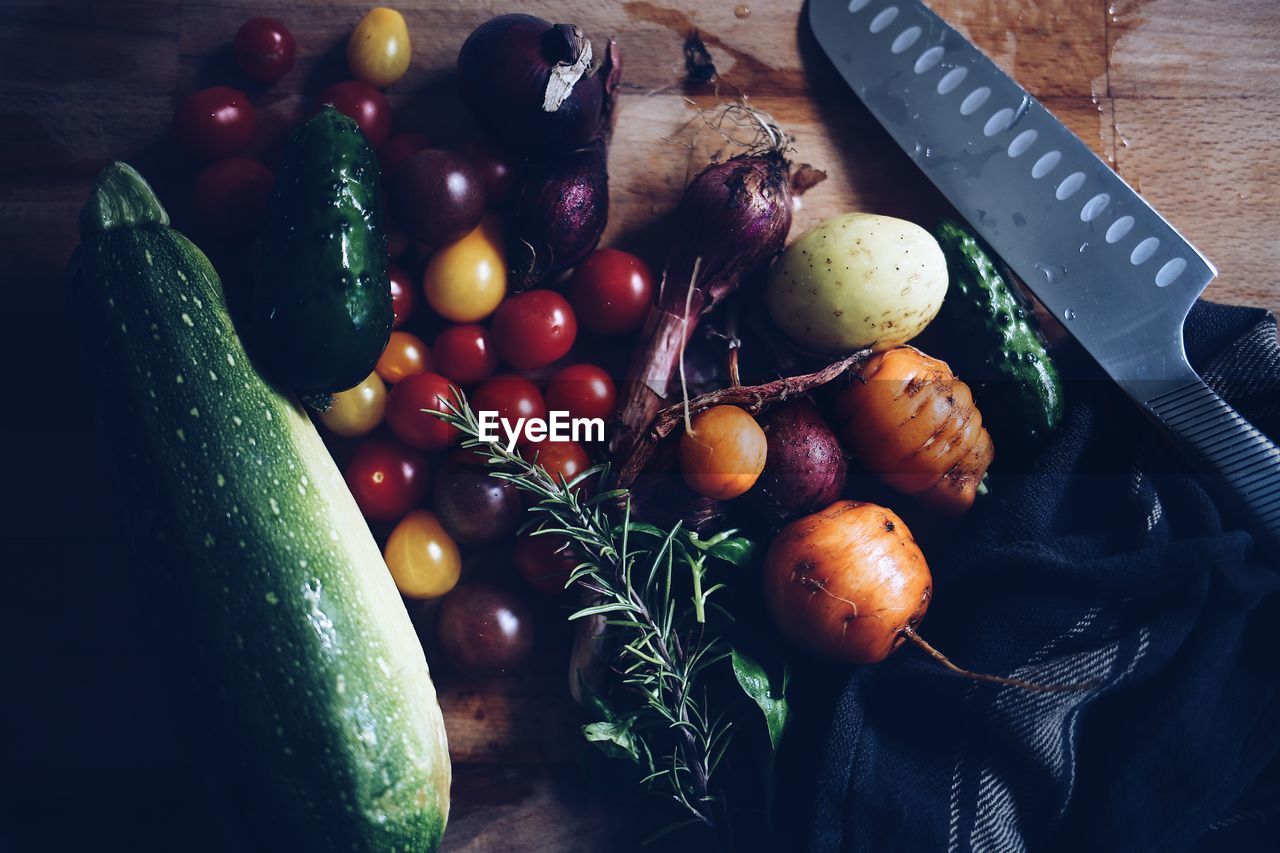 High angle view of just harvested garden products laying fresh on a wooden table beside a knife 