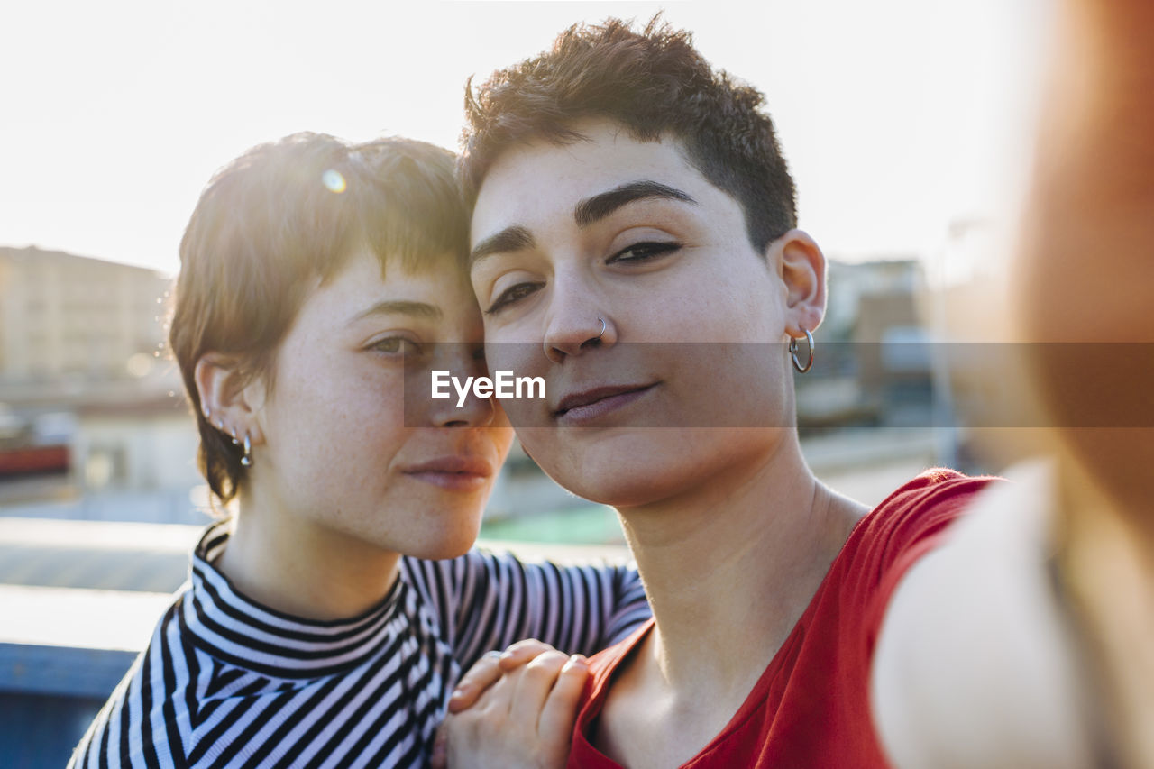 Close-up portrait of confident lesbian couple standing against clear sky in city