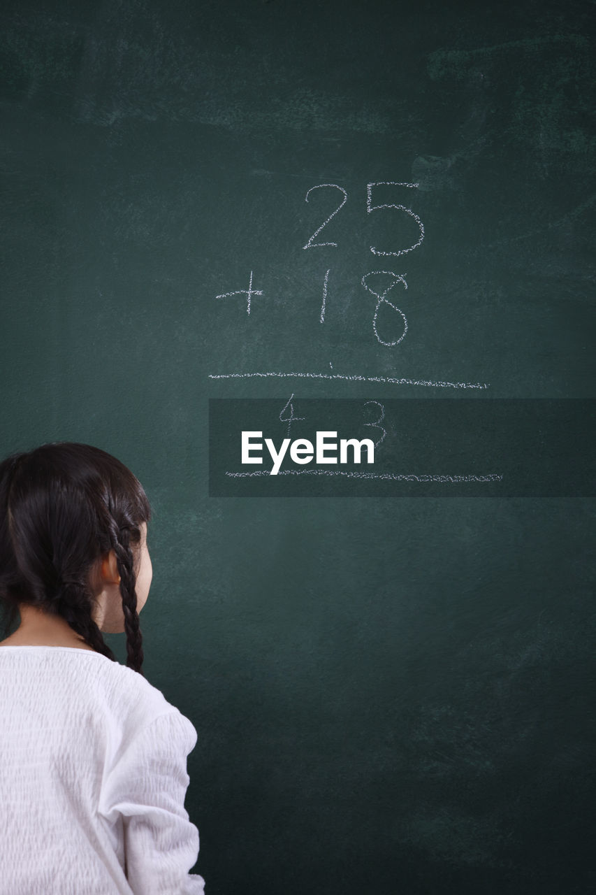 Rear view of girl learning mathematics on blackboard