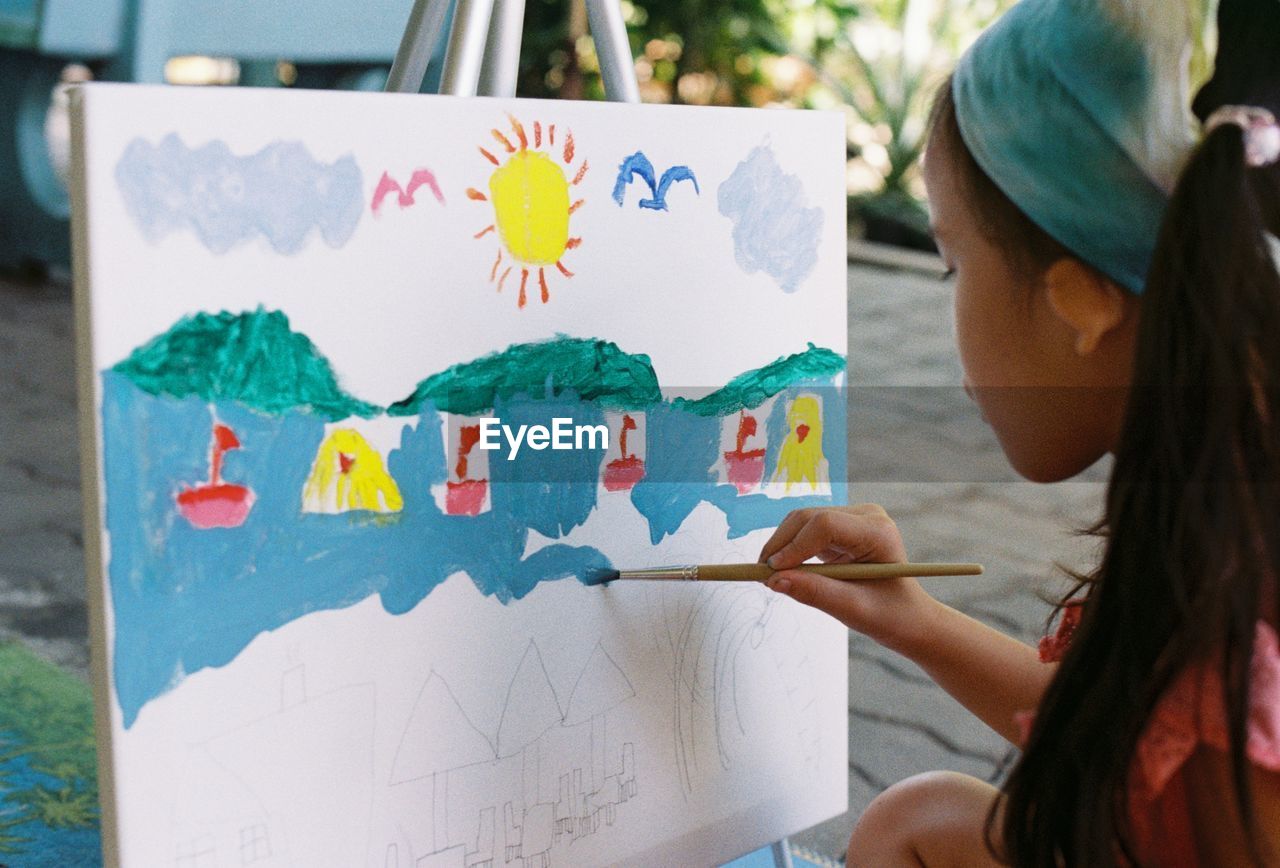 Close-up of girl painting on canvas outdoors