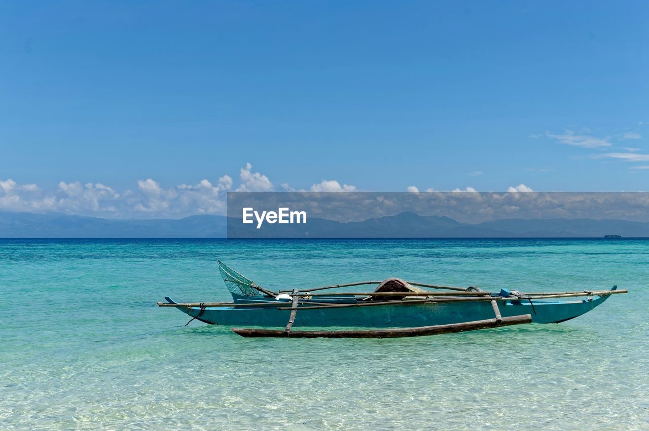 Outrigger canoe moored on sea against sky