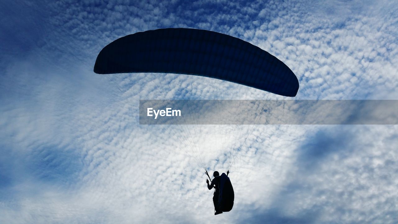 Low angle view of silhouette person paragliding against sky