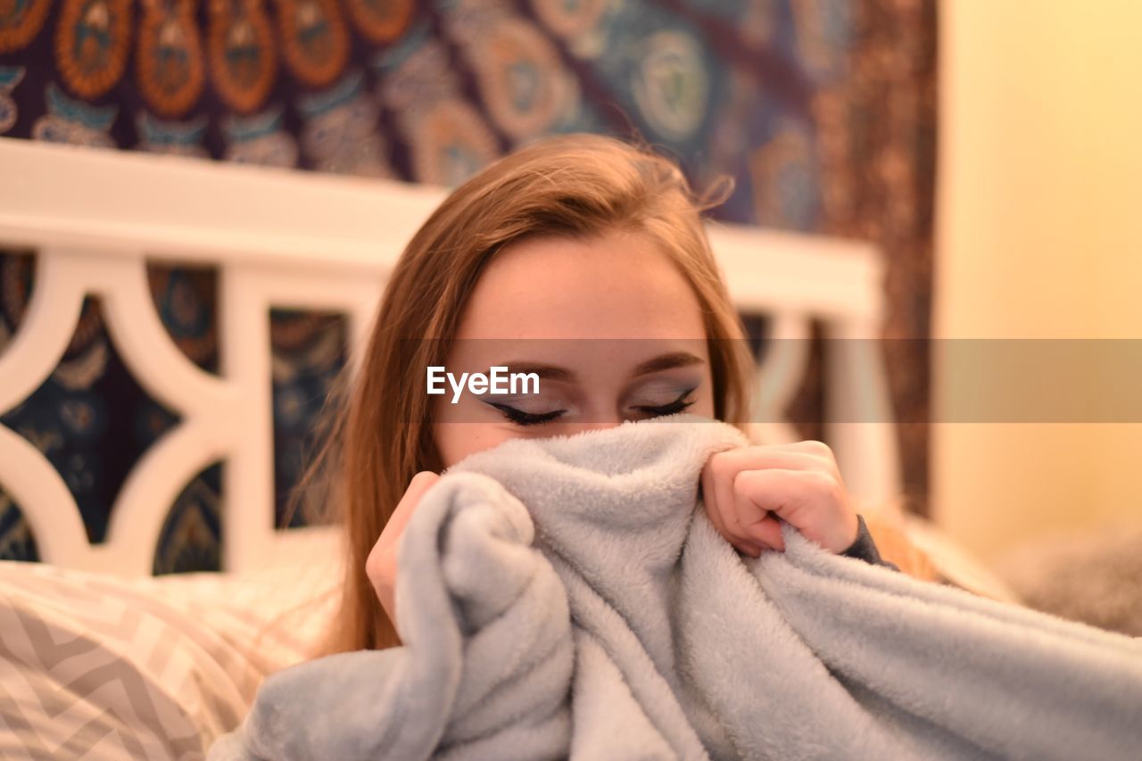 Close-up of teenage girl holding blanket on bed at home