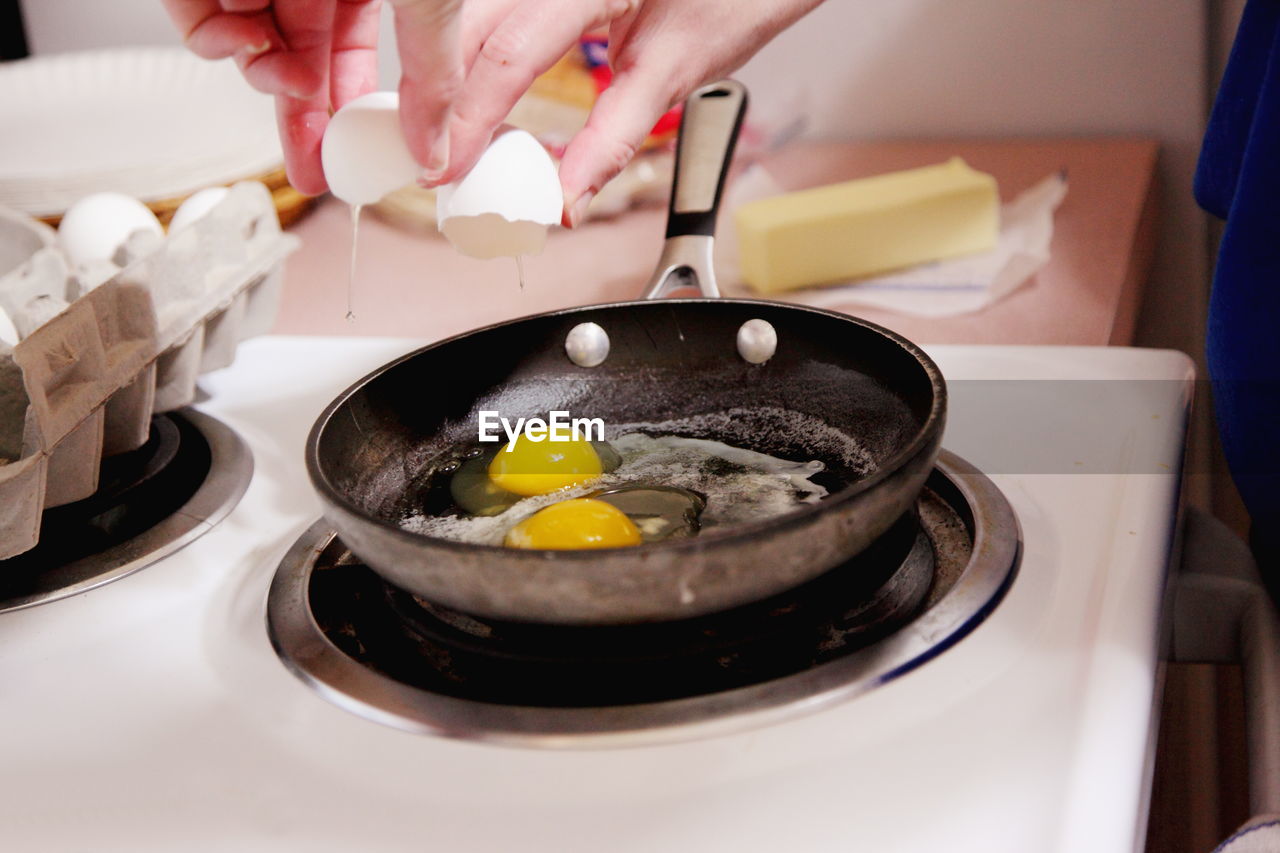 Cropped image of woman breaking egg on frying pan in kitchen