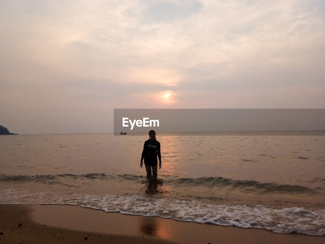 REAR VIEW OF MAN STANDING AT BEACH DURING SUNSET