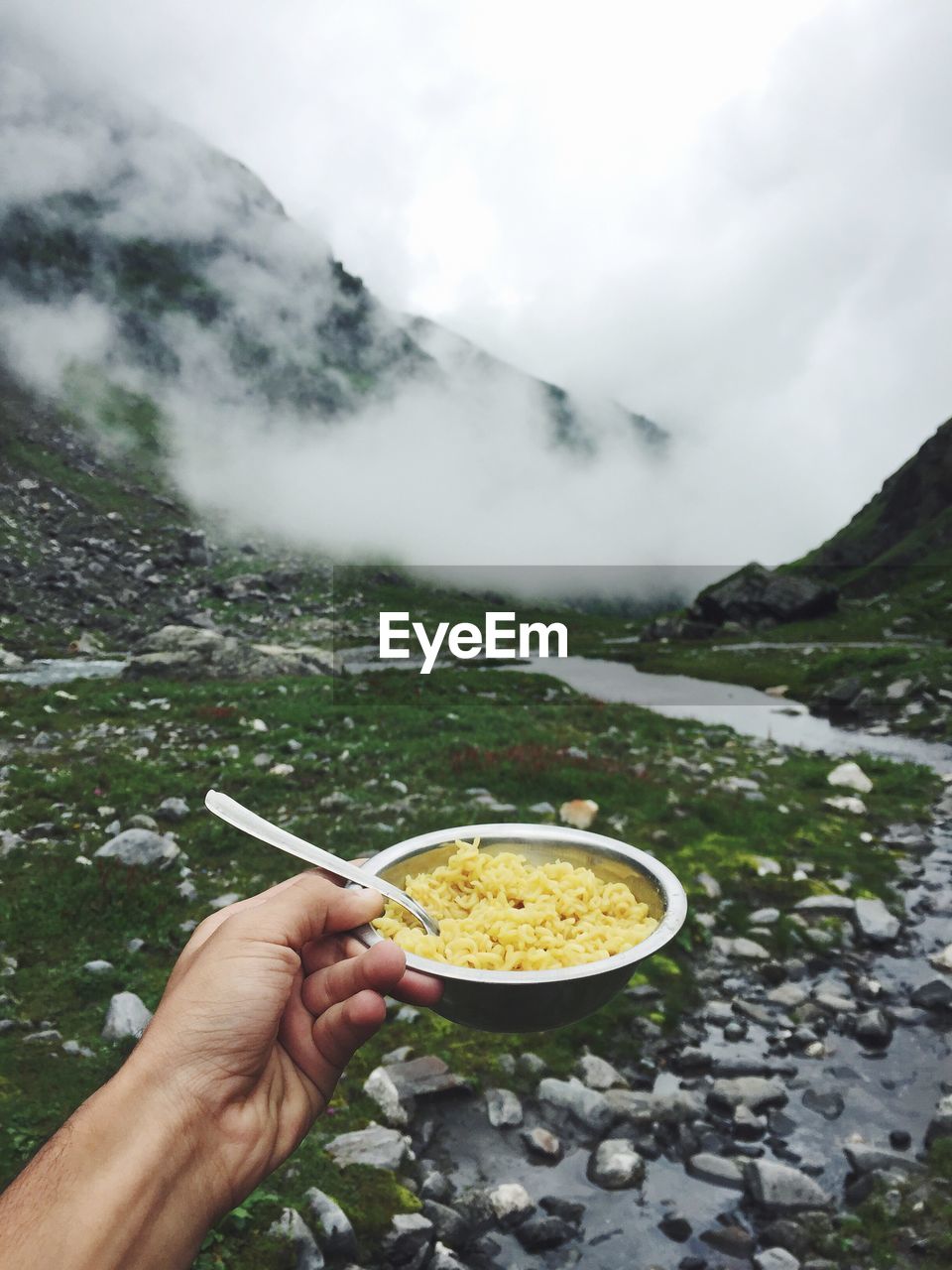 Close-up of cropped hand holding noodles in bowl against mountains at manali