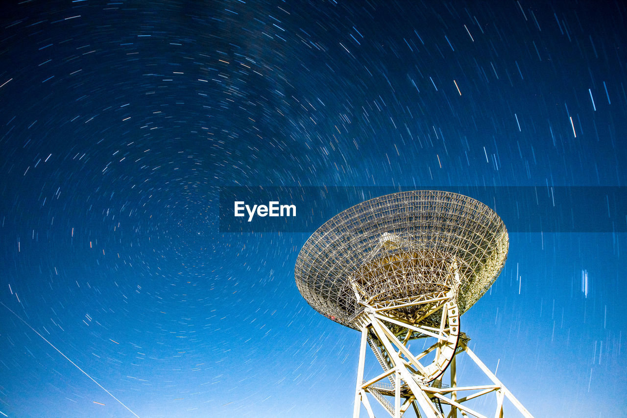 Low angle view of satellite dish against star trails at dusk