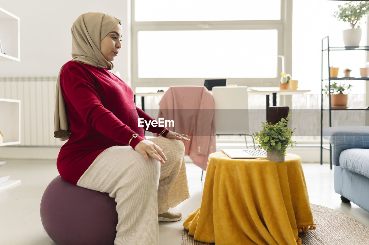 Pregnant woman learning online yoga on laptop in living room