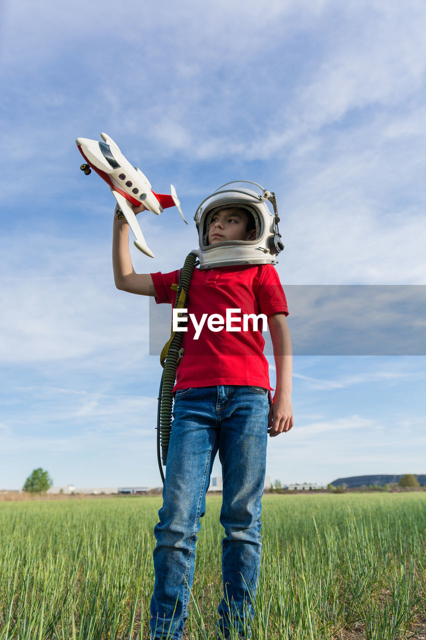 REAR VIEW OF BOY STANDING ON FIELD