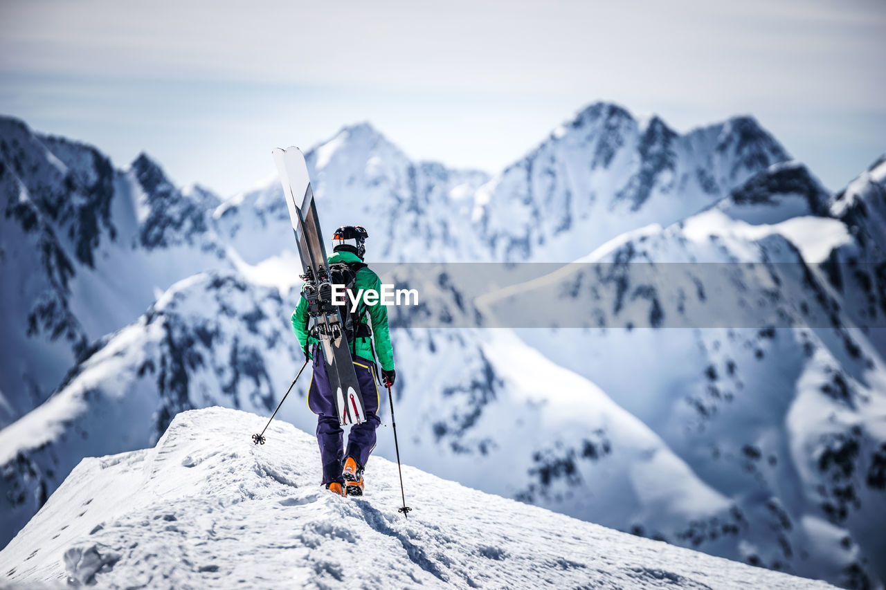 Man hiking on snowcapped mountain peak while looking at landscape against sky