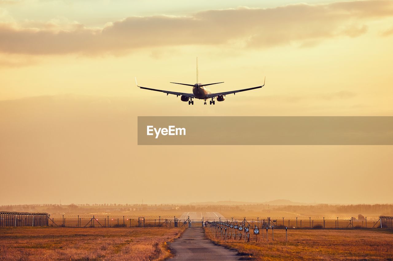 Airplane flying over road against sky during sunset