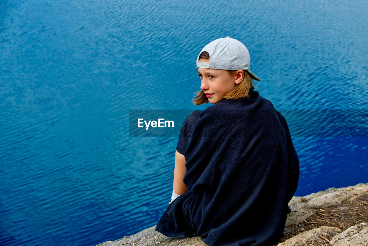 Rear view of girl sitting on rock against sea