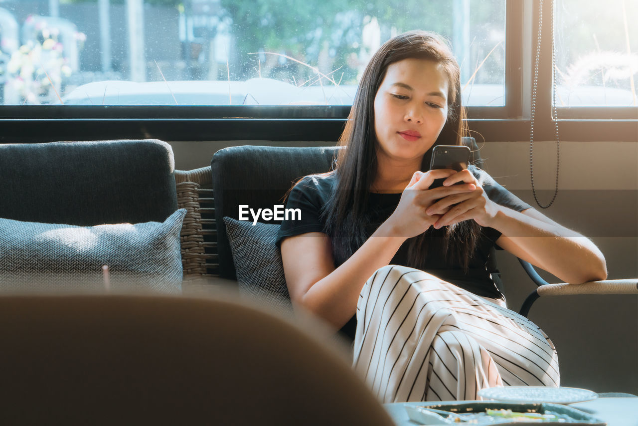 Woman using mobile phone while sitting on window