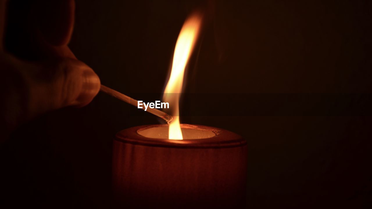 Close-up of hand holding illuminated matchstick over candle