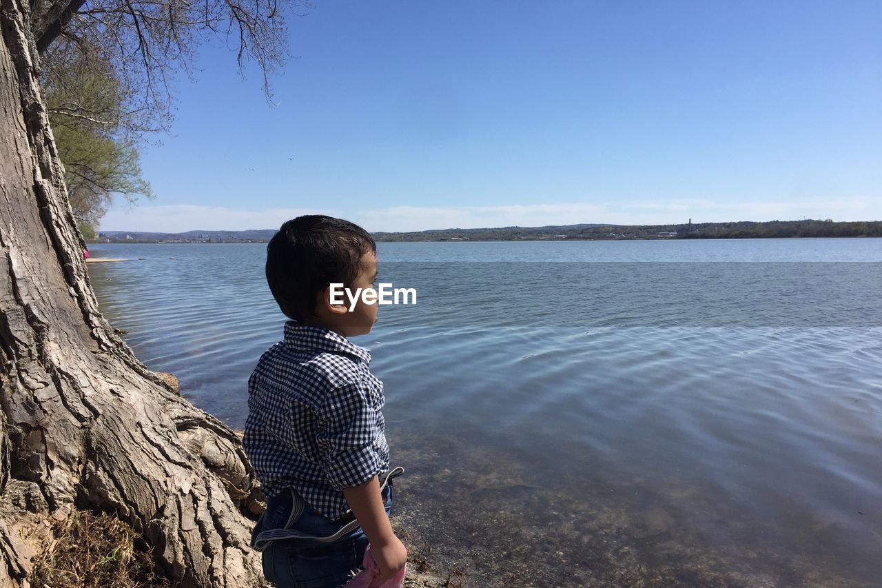 Boy standing at riverbank against sky