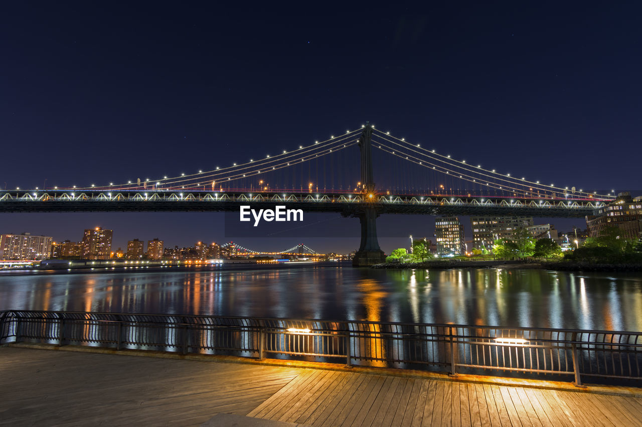 Illuminated manhattan bridge over east river against sky seen from pier