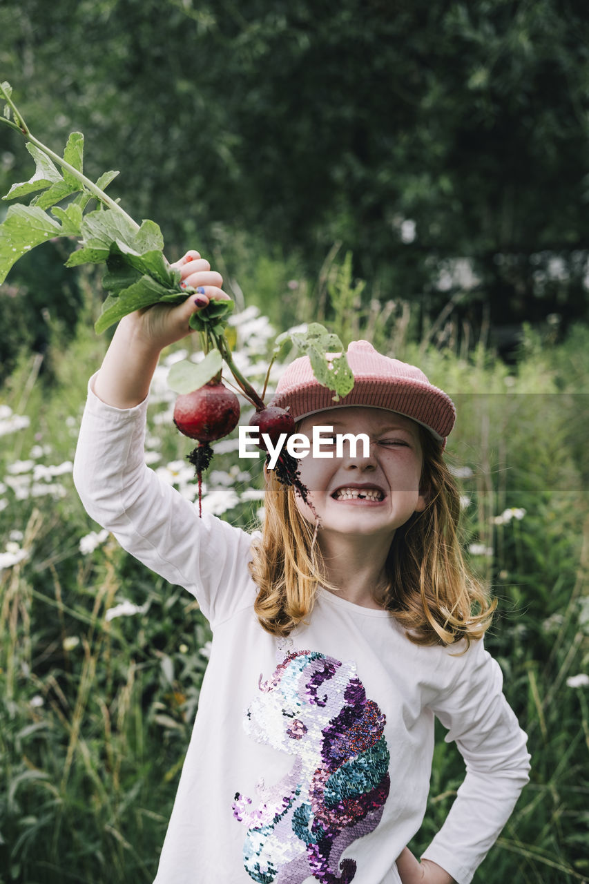 Innocent blond girl with beetroots standing in vegetable garden