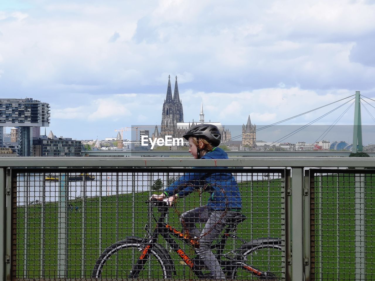 MAN RIDING BICYCLE ON BRIDGE IN CITY AGAINST SKY