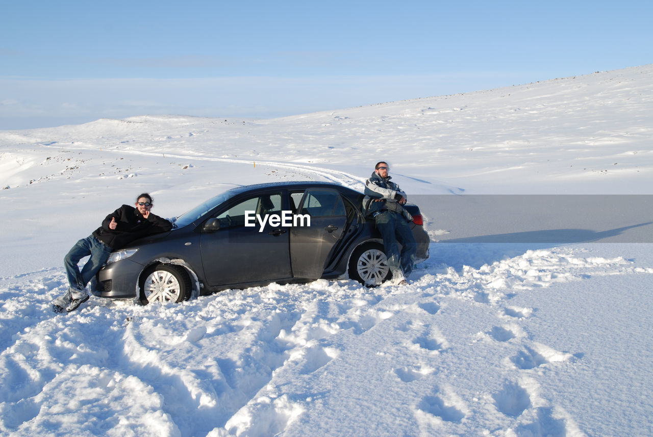Male friends standing by car on snow covered field